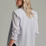 Woman wearing a light  textured shirt with rolled-up sleeves on a plain background