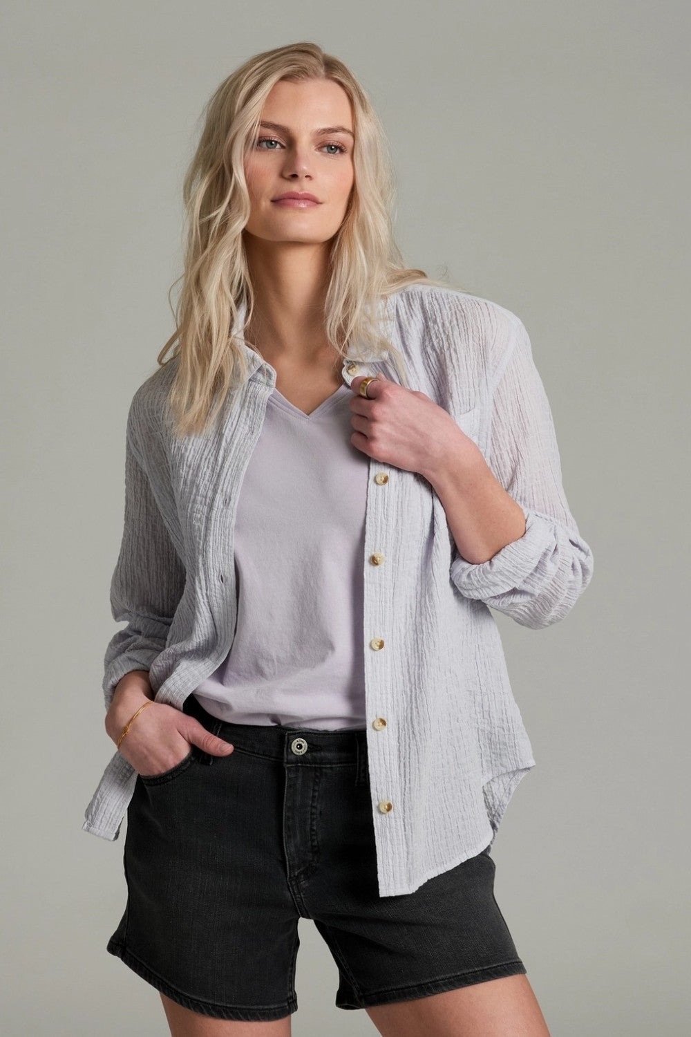 Woman wearing a light  button-up shirt over a light shirt with black shorts on a gray background