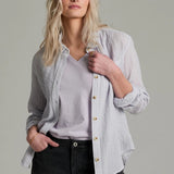 Woman wearing a light  button-up shirt over a light shirt with black shorts on a gray background