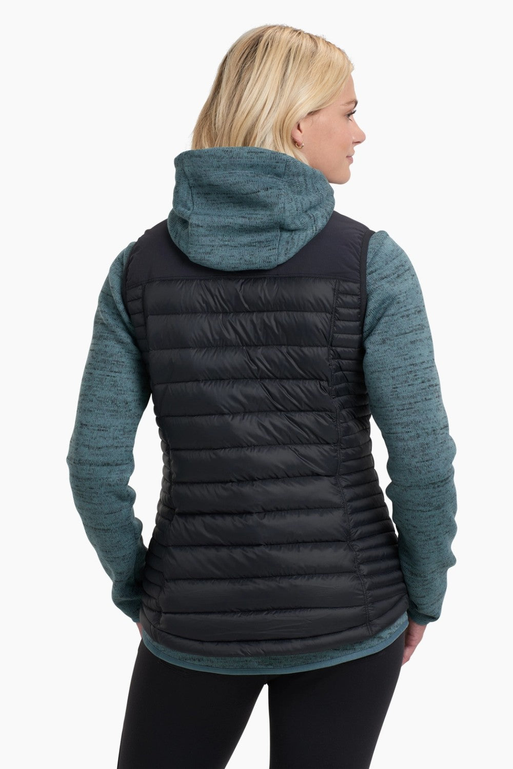 Woman wearing a black puffer vest over a teal and black sweater on a white background