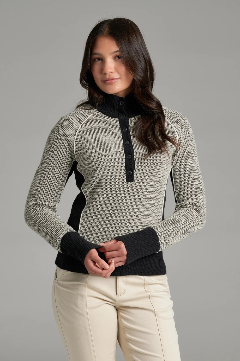 A woman wearing a textured gray and black knit sweater with a black collar and button placket, photographed against a light grey backdrop.