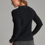 Woman, shown from the back, wearing a black sweater and black jeans against a light grey backdrop.