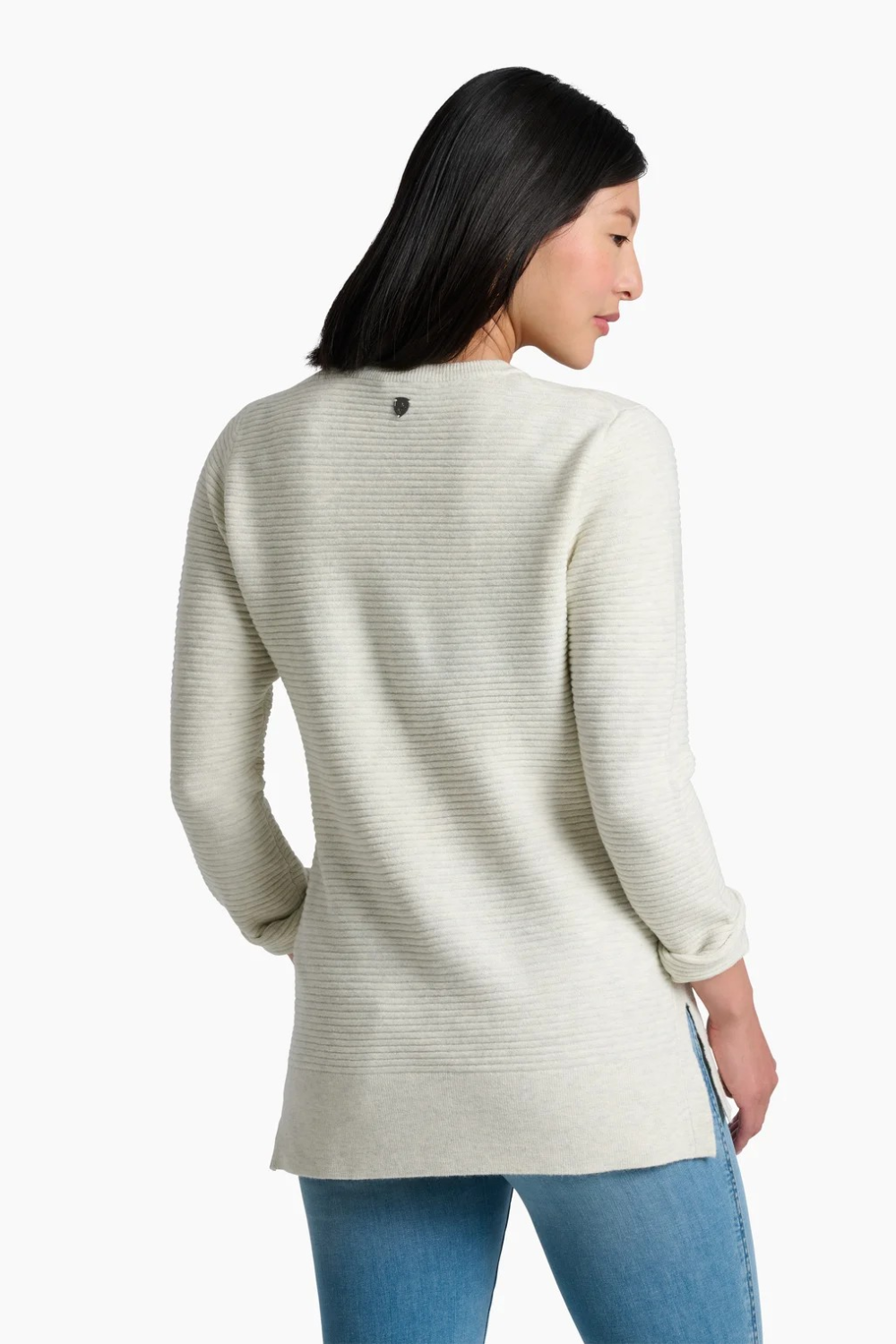 A woman wearing a ribbed knit long-sleeve sweater in a light cream color, paired with blue jeans, shown from the back, against a plain white background.