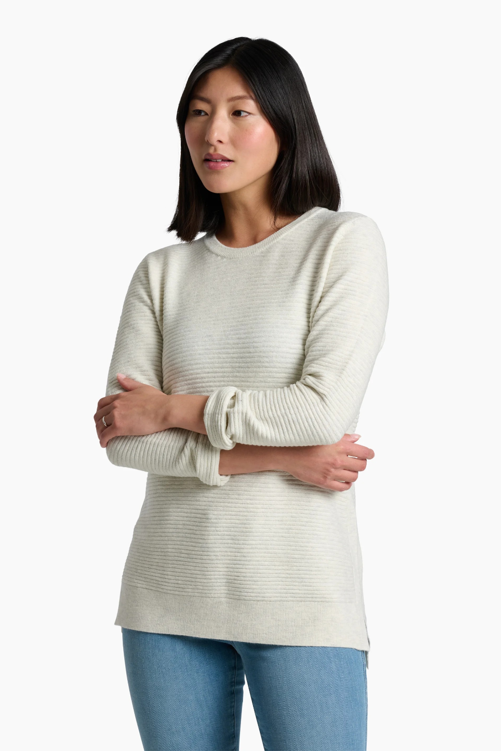 A woman modeling a cream-colored ribbed knit sweater with blue jeans against a plain white studio background.