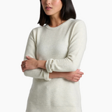 A woman modeling a cream-colored ribbed knit sweater with blue jeans against a plain white studio background.