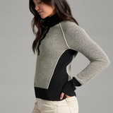 A woman, shown from the side, wearing a textured gray and black knit sweater with a black collar and button placket, photographed against a light grey backdrop.