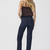 Woman, shown from the back, modelling a brown camisole with dark blue jeans and silver shoes photographed against a light background.