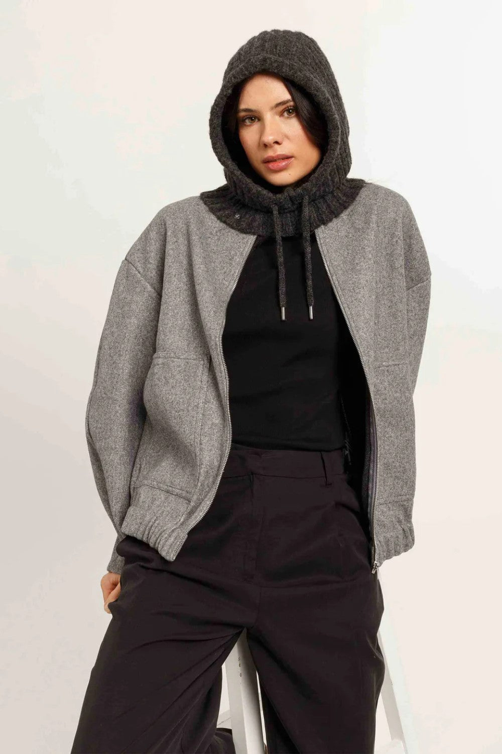 Women wearing charcoal hooded scarf with grey jacket, black T and burgundy pants on light background