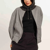 Women wearing charcoal hooded scarf with grey jacket, black T and burgundy pants on light background