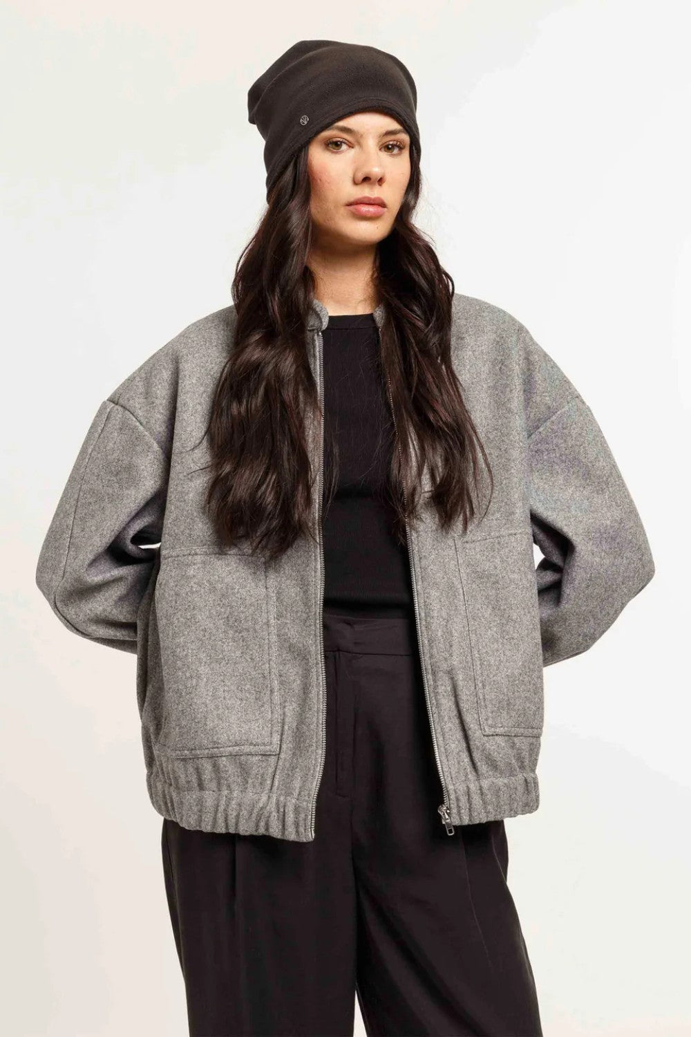 Woman wearing a gray cardigan, black top, and pants with a black beanie on a white background