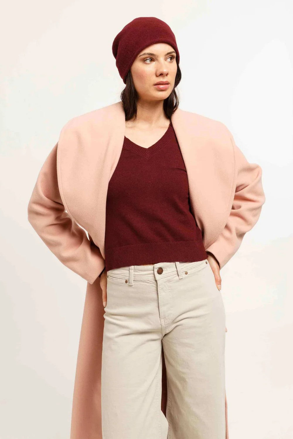 Woman wearing a pink cardigan, burgundy hat, and beige pants on a white background