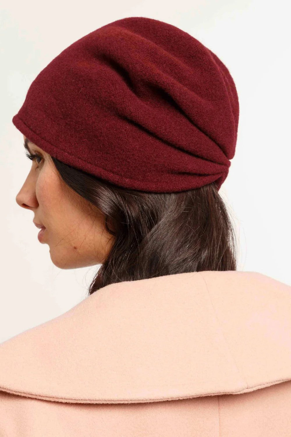 Woman wearing a burgundy hat and beige coat on a white background