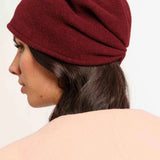 Woman wearing a burgundy hat and beige coat on a white background
