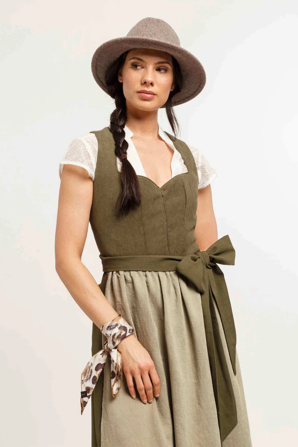 Woman wearing a green dress with a beige skirt and a tan hat on a white background