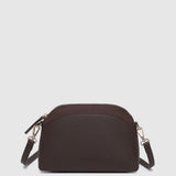 A dark brown pleather crossbody bag with a curved top and a small embossed logo on the front, shown against a light gray background.