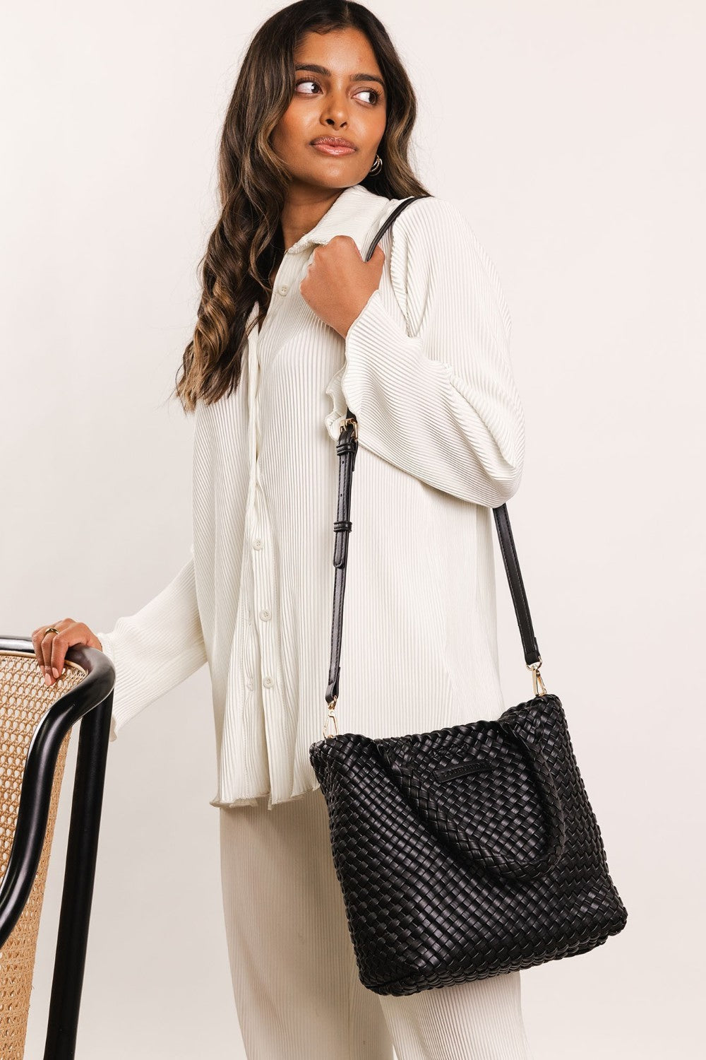Black woven handbag with handle and long strap worn by a woman dressed in white