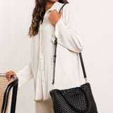 Black woven handbag with handle and long strap worn by a woman dressed in white