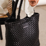 Black woven handbag with handle being held by a wrist