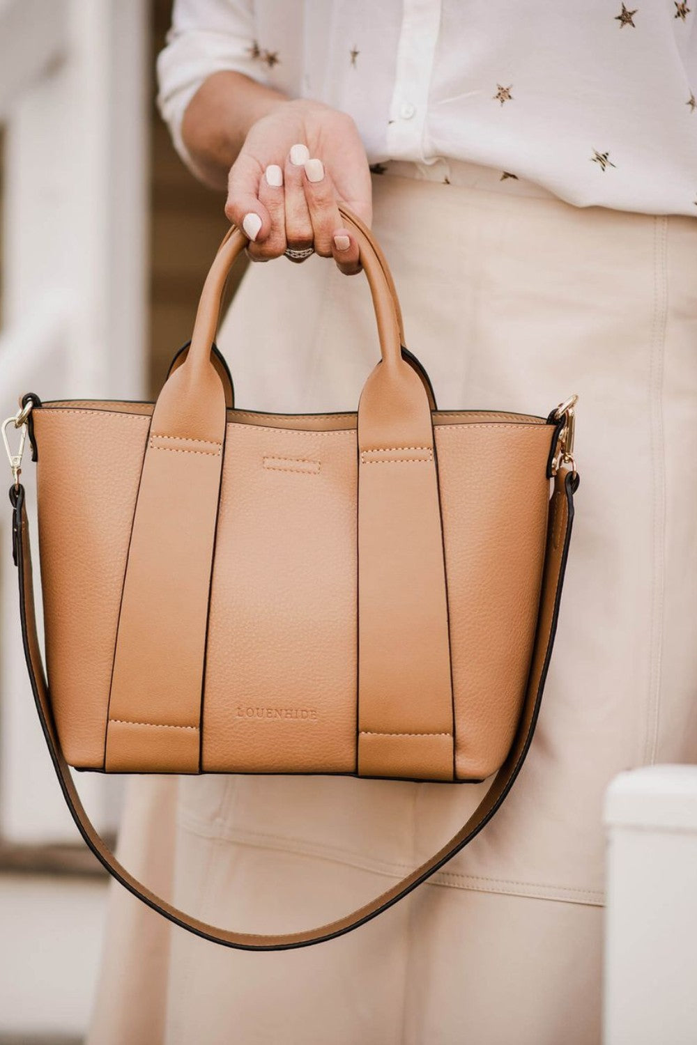 Tan handbag held by a person wearing a white blouse with star patterns.