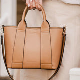 Tan handbag held by a person wearing a white blouse with star patterns.