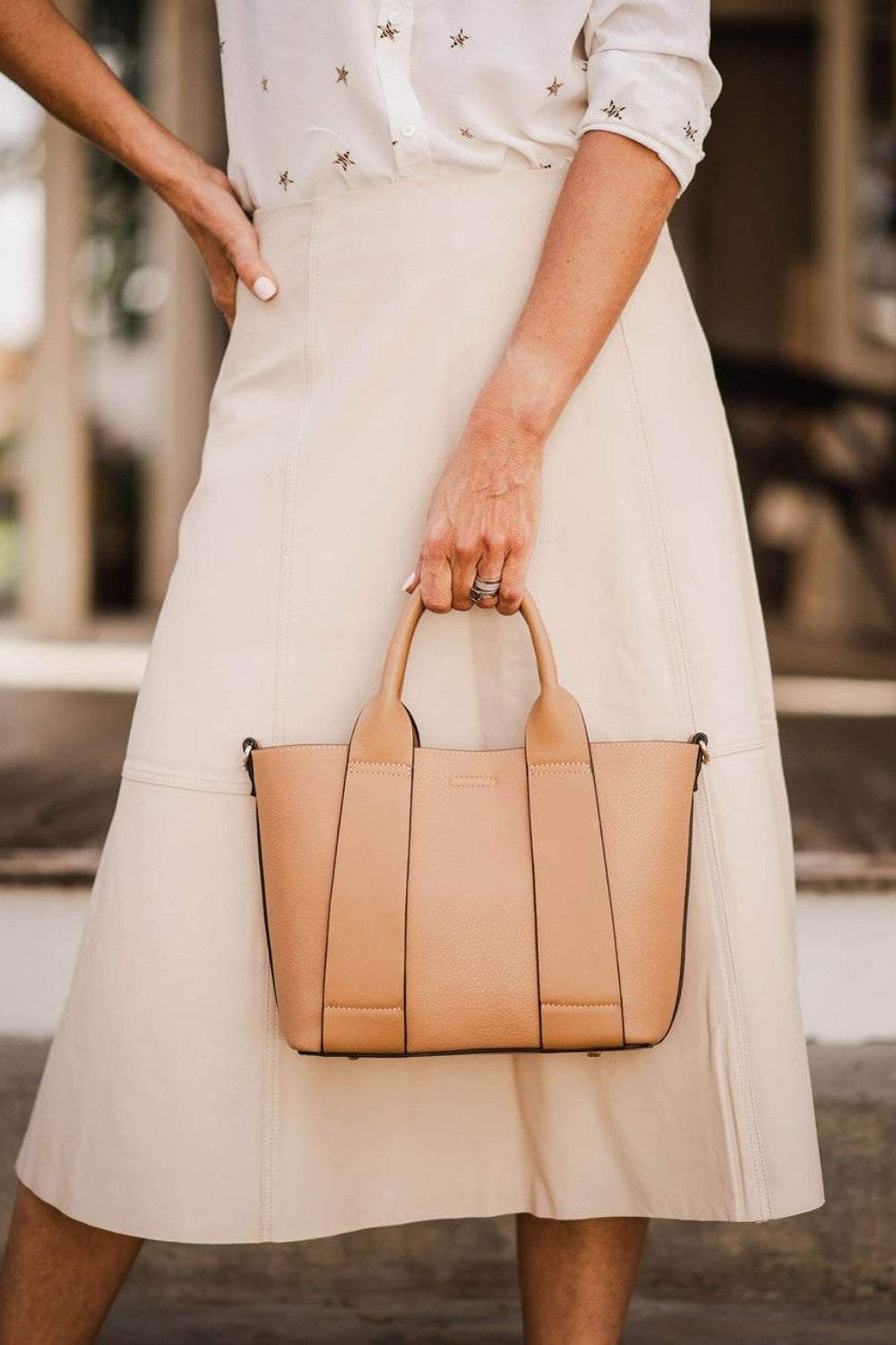 Person holding a beige handbag wearing a white skirt and blouse.
