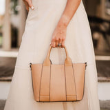 Person holding a beige handbag wearing a white skirt and blouse.