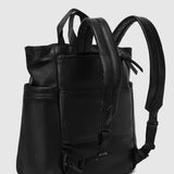 A black pebbled leather backpack with dual top handles and adjustable shoulder straps, shown from a three-quarter angle against a light gray background.