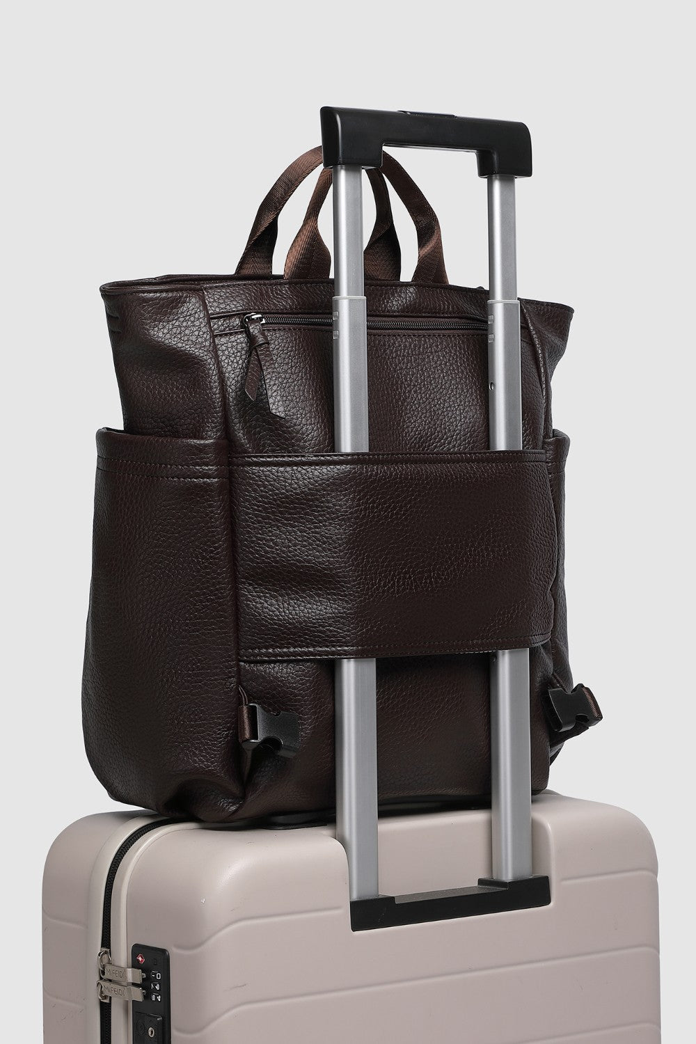 Brown pleather bag with handle and strap on top of a beige suitcase.