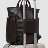 Brown pleather bag with handle and strap on top of a beige suitcase.