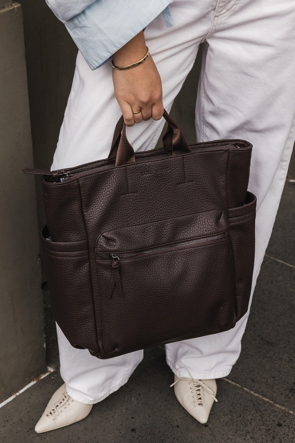 Person holding a brown pleather bag against a neutral background