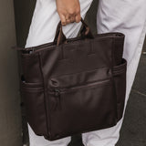 Person holding a brown pleather bag against a neutral background