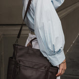 Person wearing a light blue jacket and white pants, holding a brown pleather bag.