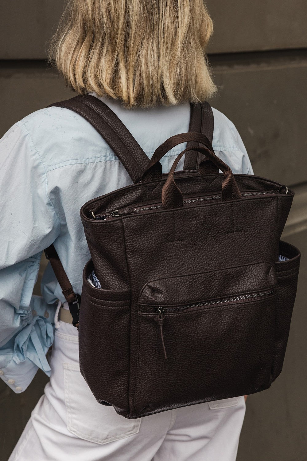 Person wearing a brown pleather backpack with a neutral background