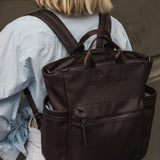 Person wearing a brown pleather backpack with a neutral background