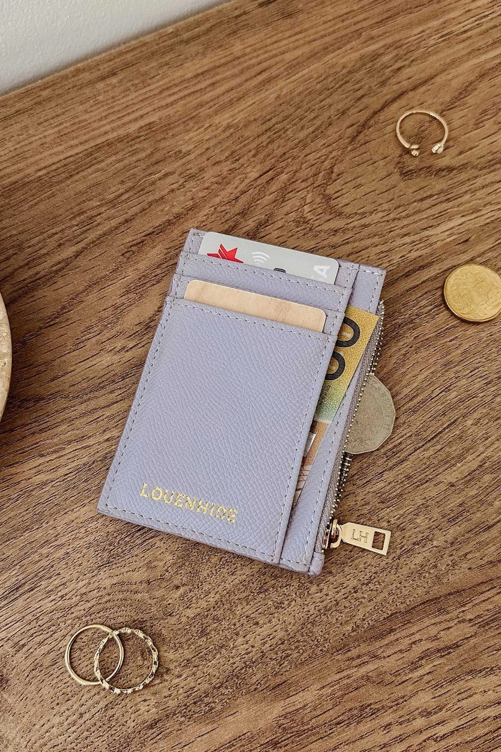 Lilac wallet with card slots and coins on a wooden surface
