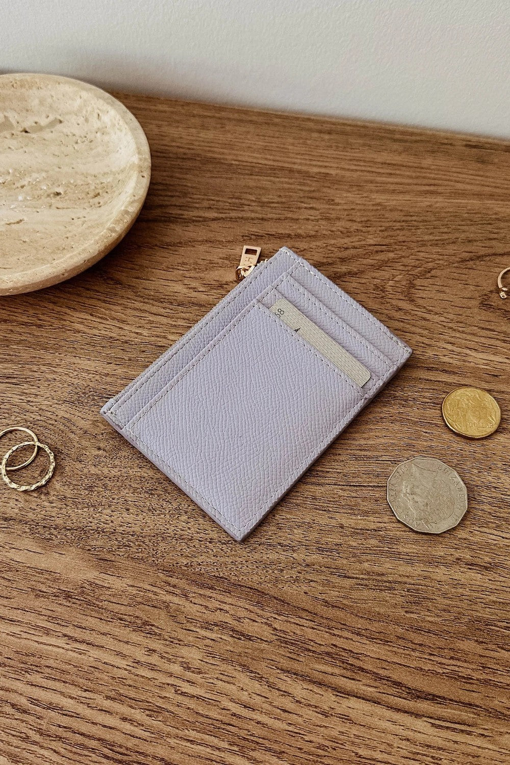 Lilac wallet with card slots and coins on a wooden surface