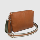 A brown leather crossbody bag with a tassel detail and a wide, striped adjustable shoulder strap, shown against a light gray background.
