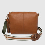 A brown leather crossbody bag with a wide woven strap featuring green, white, and brown stripes, and a tassel detail on the side, shown against a light gray background.