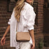 Woman in a white outfit with a beige handbag standing against a brick wall.
