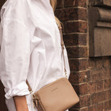 Person wearing a white shirt with a beige handbag against a brick wall.