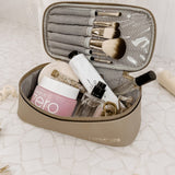 Makeup set with brushes, bottles, and jars in a beige travel case on a textured white surface.