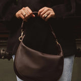 Person holding a brown leather handbag with a blurred background