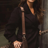 Woman holding a brown leather bag against a dark background