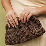 Person holding a brown woven clutch with a blurred background