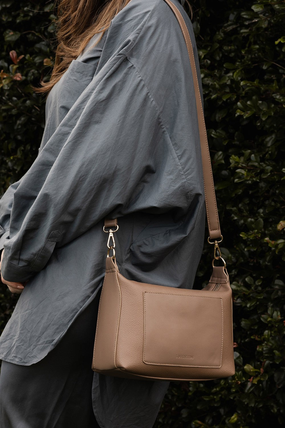 Person wearing a gray jacket with a brown pleather handbag against a dark background