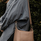 Person wearing a gray jacket with a brown pleather handbag against a dark background