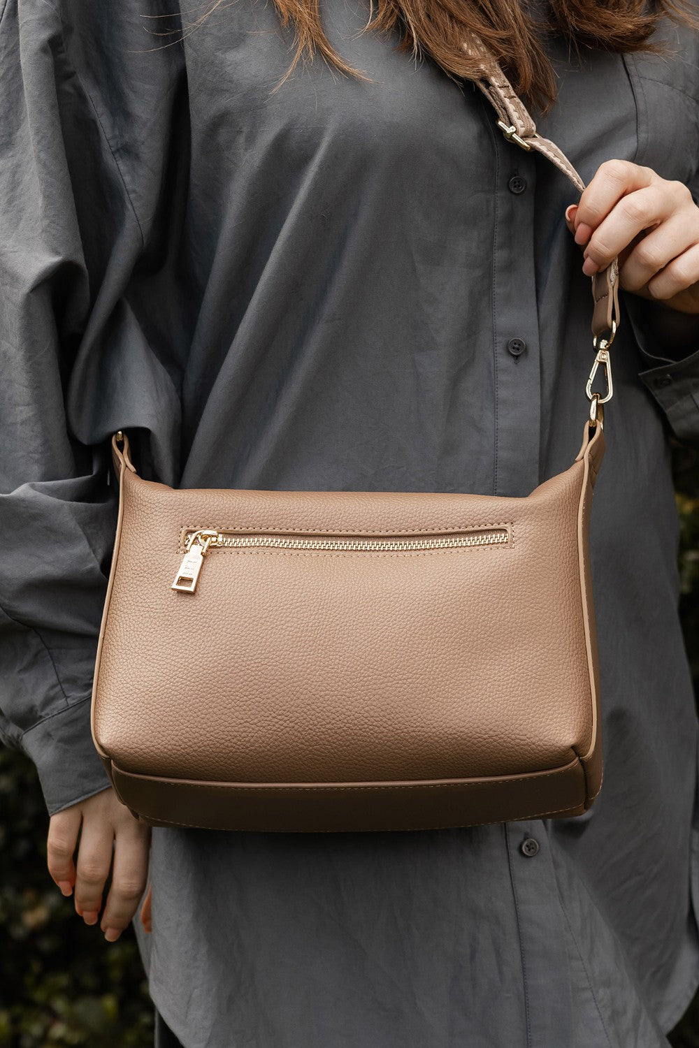 Person holding a brown pleather handbag with a blurred background