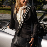 Woman holding a black handbag next to a car