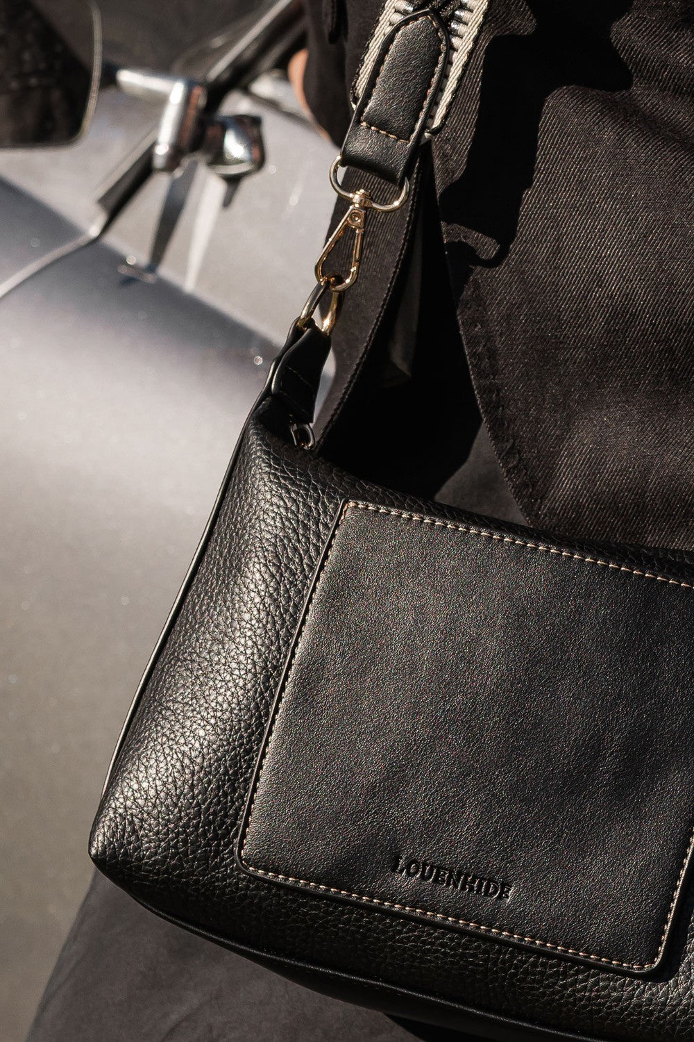 Black pleather handbag with 'LOUENHIDE' branding on a blurred background