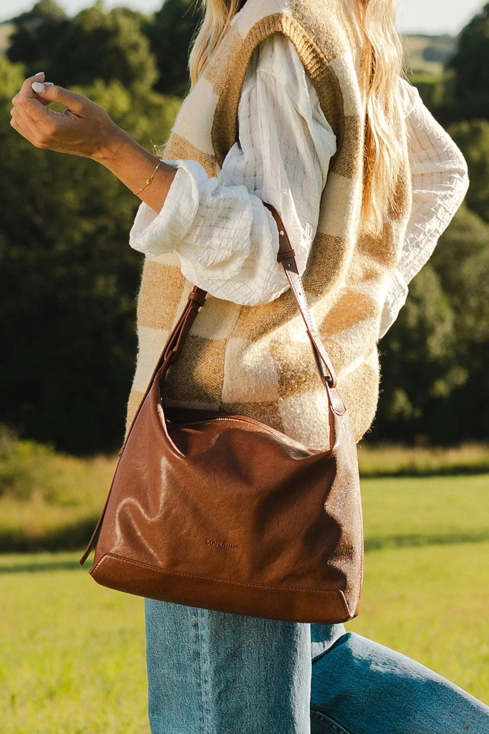 Person holding a brown leather bag outdoors in a natural setting